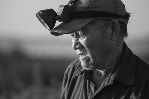 Grayscale Photo of an Elderly Man with a Flashlight on His Cap