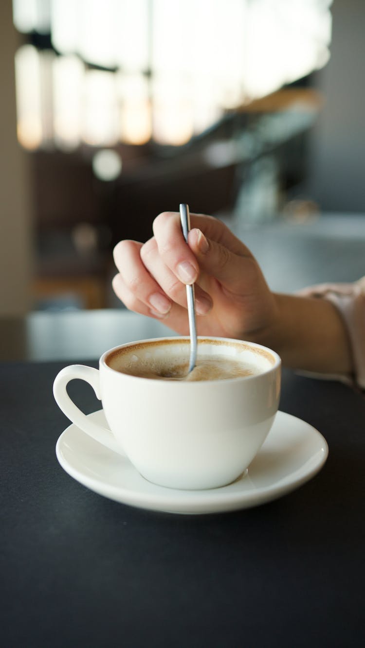 Person Stirring Coffee In A White Ceramic Cup