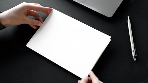 Person Holding a White Paper Beside a Pen