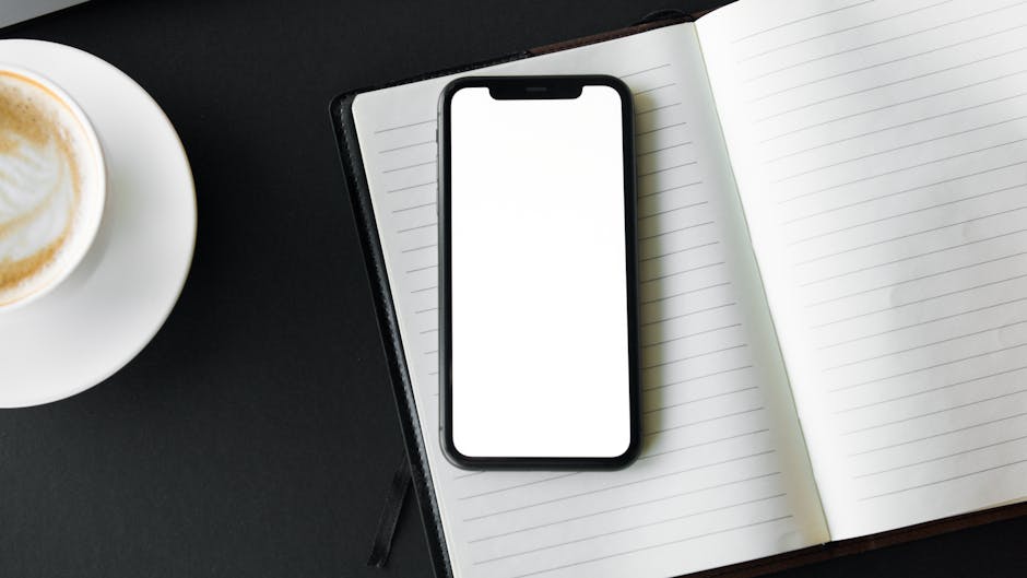 Overhead shot of a smartphone and coffee on a desk with a notebook. Perfect for work and tech themes.