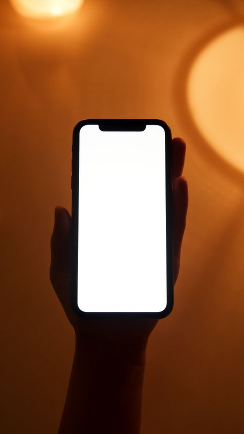 Free Vertical shot of a hand holding a smartphone with a blank white screen in a warm indoor setting. Stock Photo