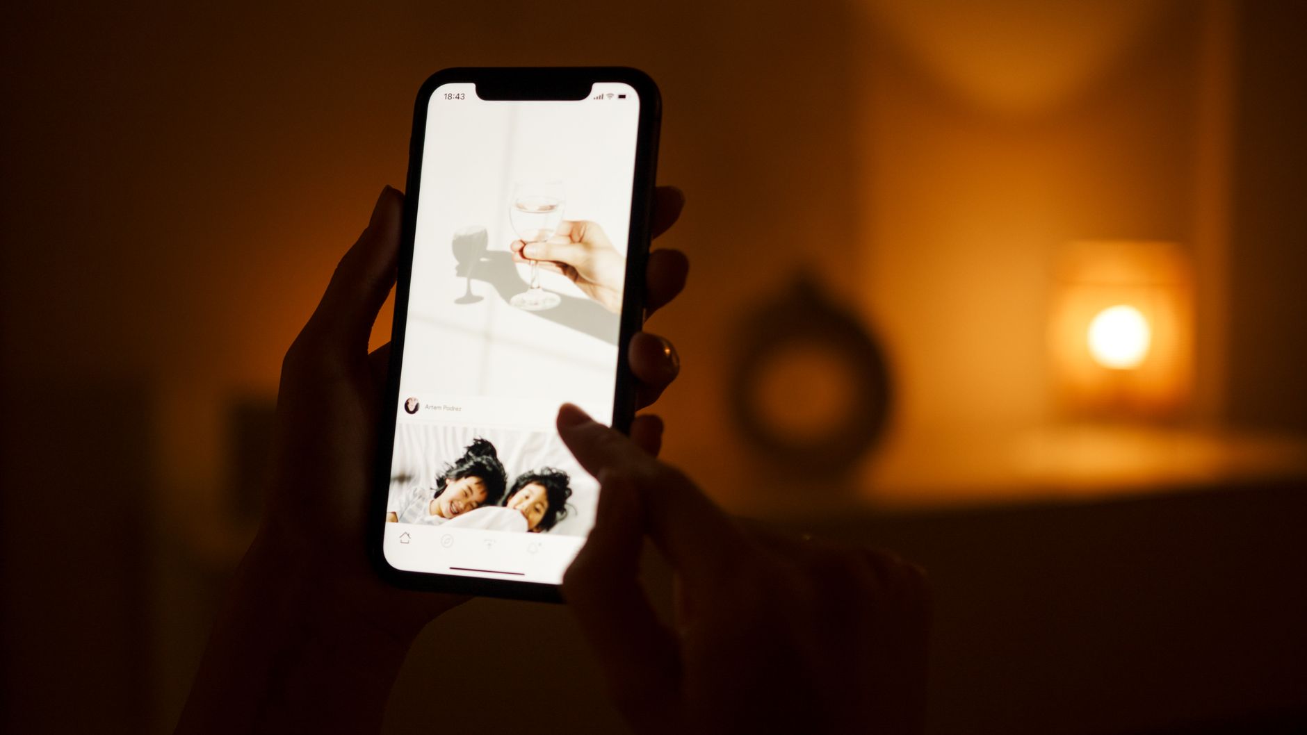 A person holds a smartphone, browsing content in a cozy dim-lit room, capturing a warm atmosphere.