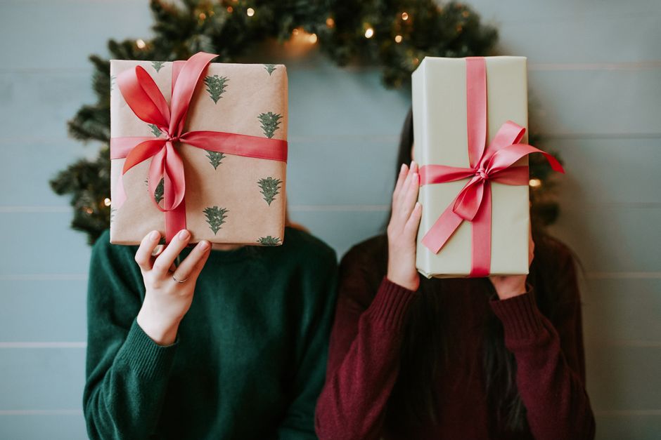 Two people holding Christmas gifts in front of a festive wreath indoors.