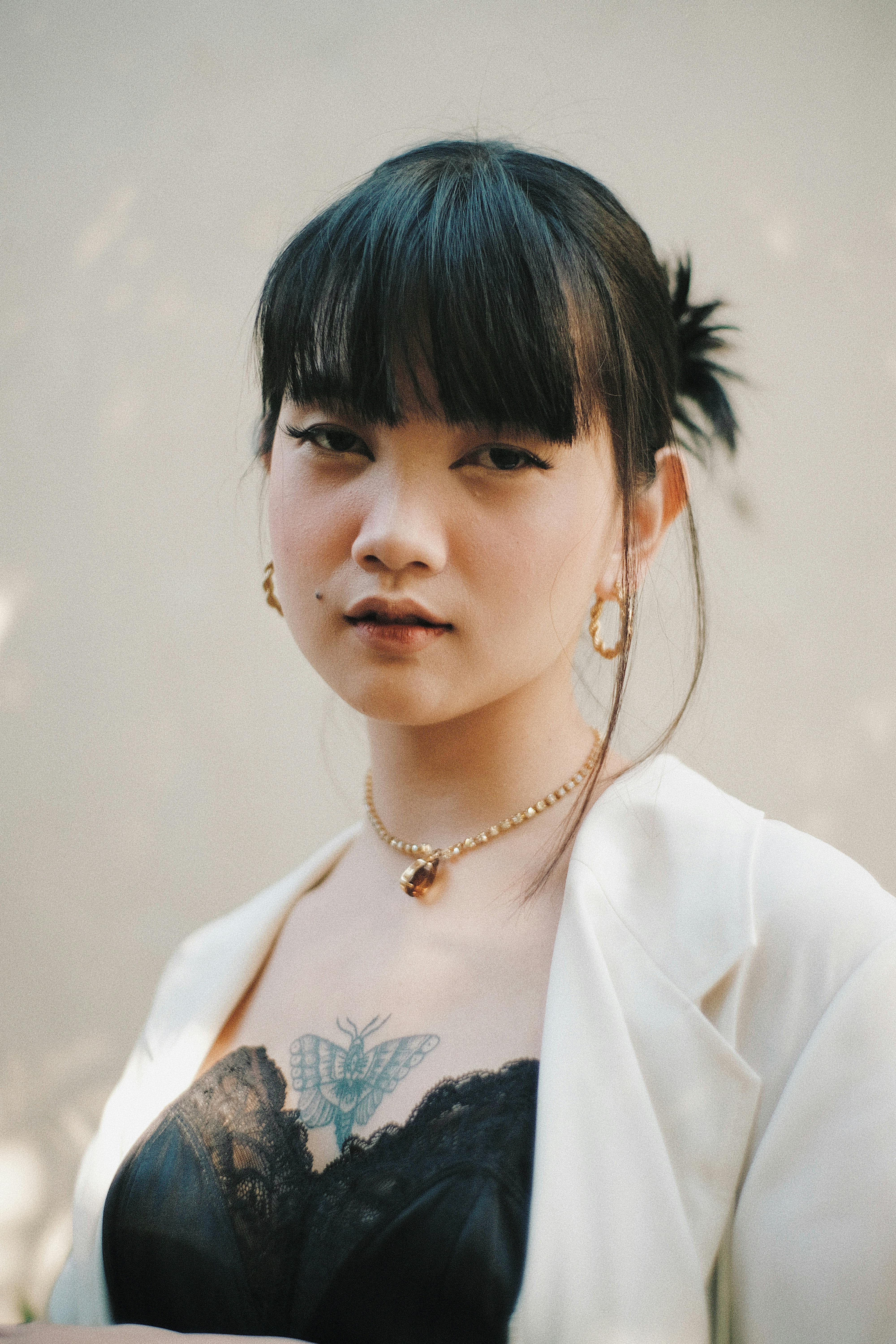 Calm young ethnic lady with butterfly tattoo on chest and piercing outfit looking at camera