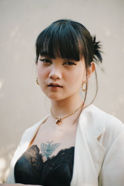Calm young ethnic lady with butterfly tattoo on chest and piercing outfit looking at camera