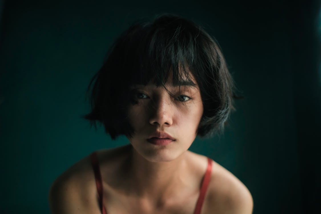 Sad young Asian female in red top looking at camera in studio with green wall