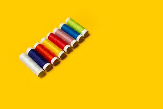 From above set of different colored thread spool arranged in row on bright yellow background