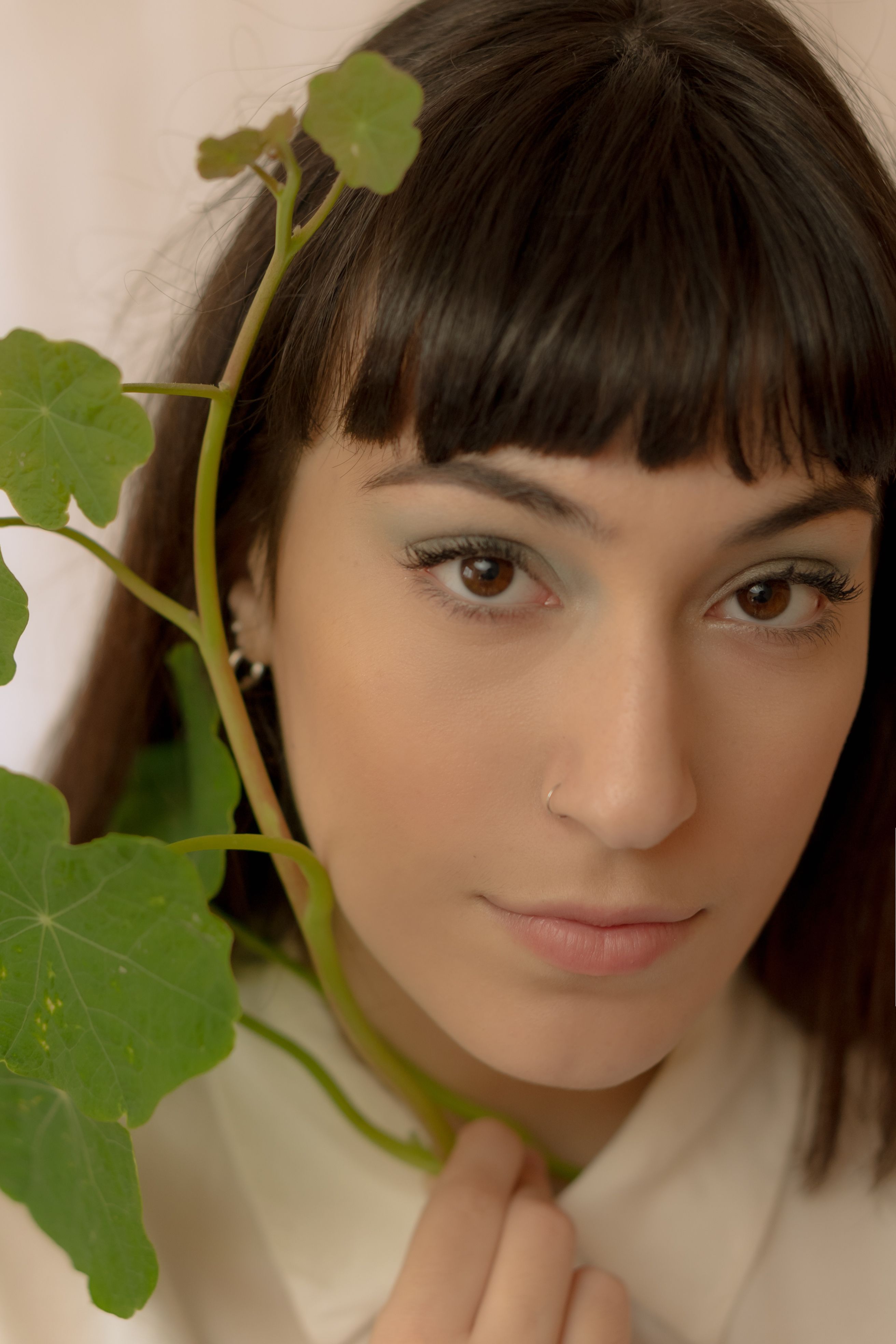 Close-up portrait of a woman holding green leaves indoors, showcasing natural beauty.