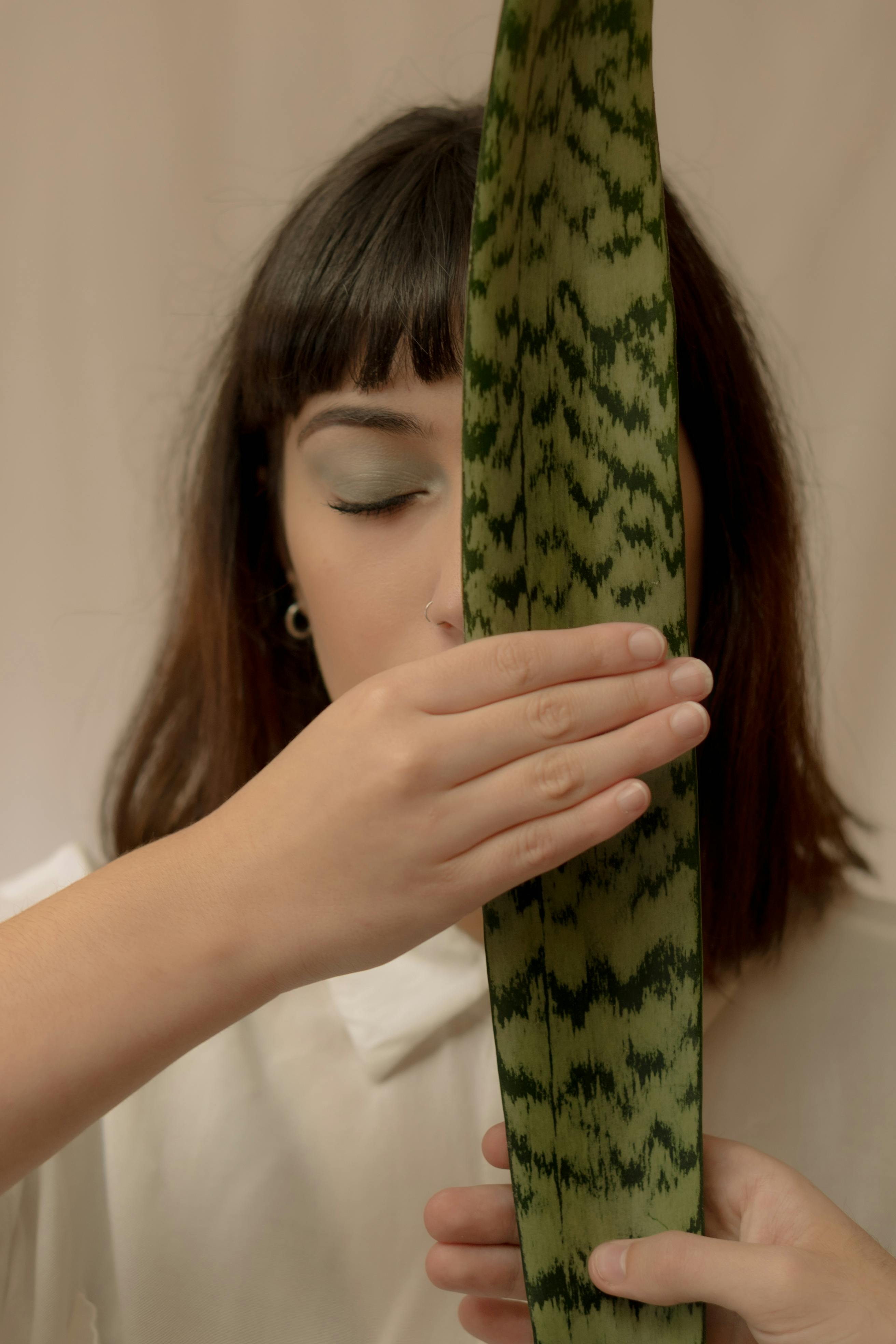 A woman with closed eyes holding a Sansevieria leaf, shot indoors in soft lighting.