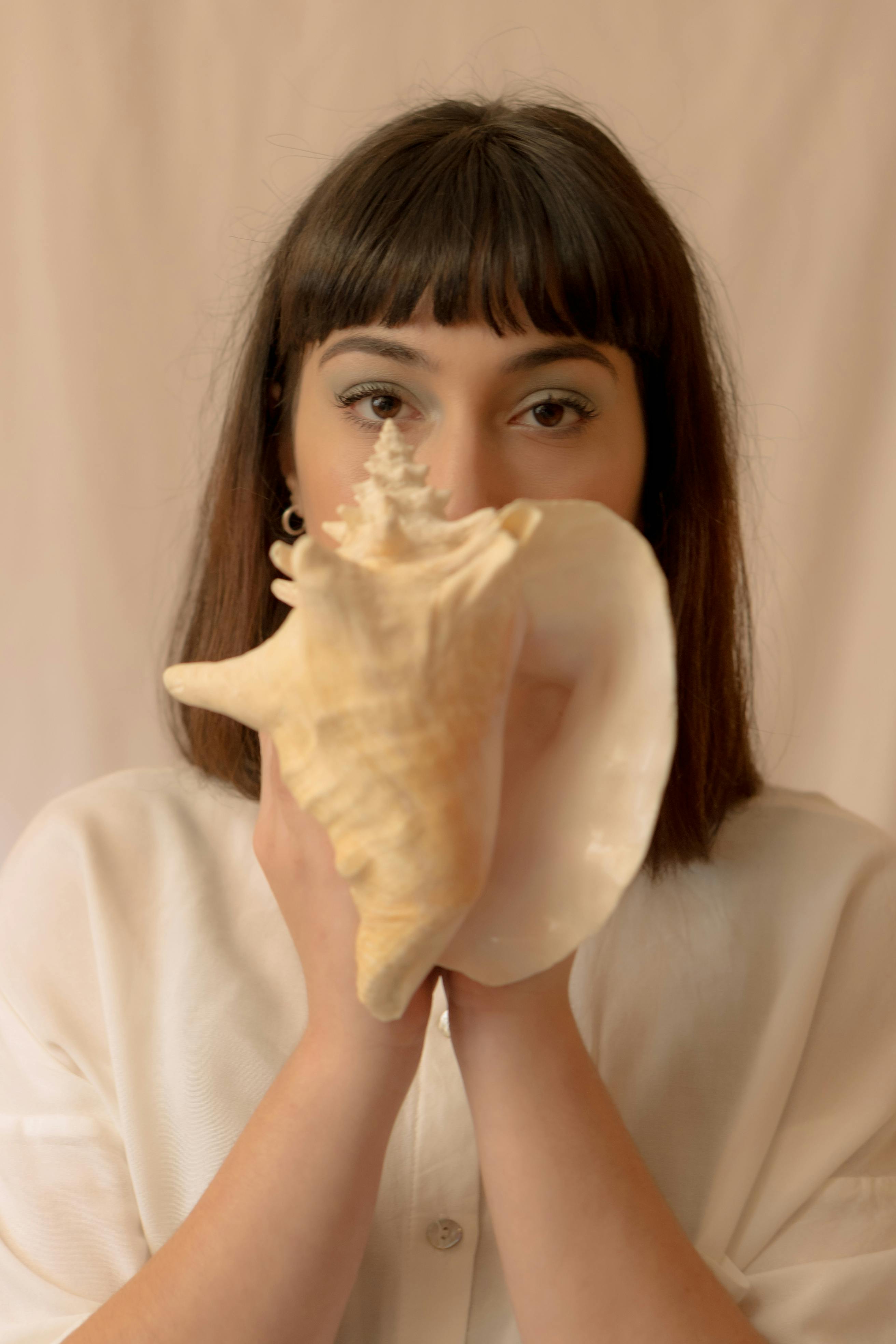 A woman holding a seashell up to her face, creating an artistic and intriguing portrait.