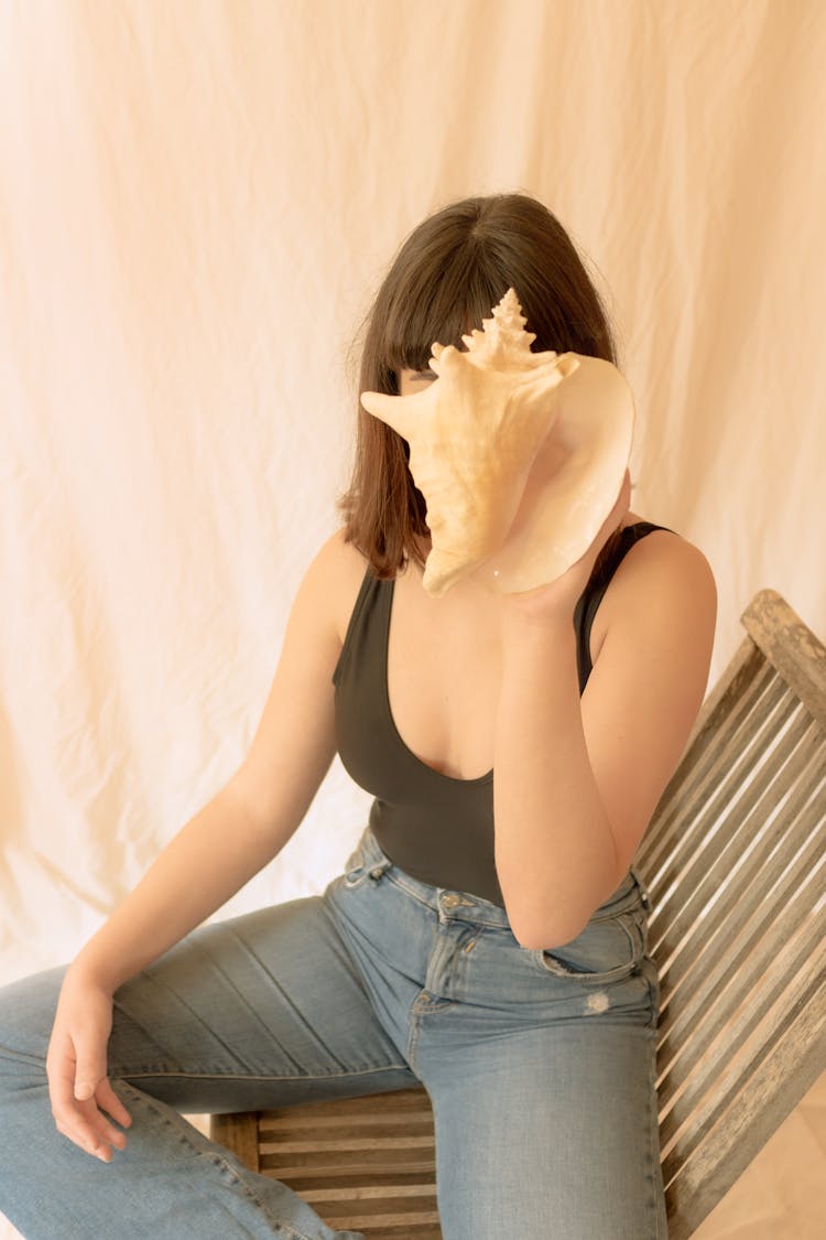 A Woman In Black Tank Top Covering Her Face With A Shell