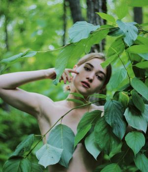 A creative portrait of a woman posing gracefully in a natural setting, surrounded by vibrant green foliage.