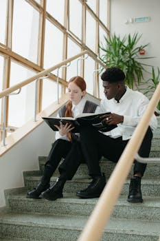 Two young students reading a book on indoor stairs, symbolizing education and diversity.
