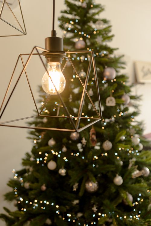 Free Stylish Christmas light bulb against a beautifully decorated tree Stock Photo