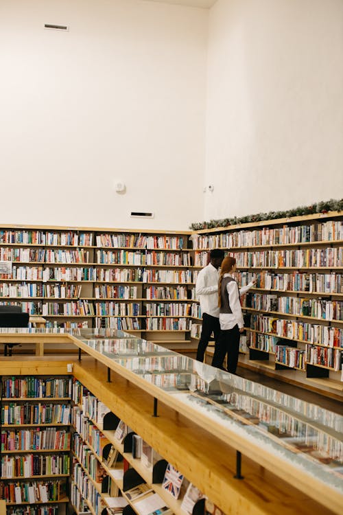 A Man and Woman Standing Near the Bookshelves