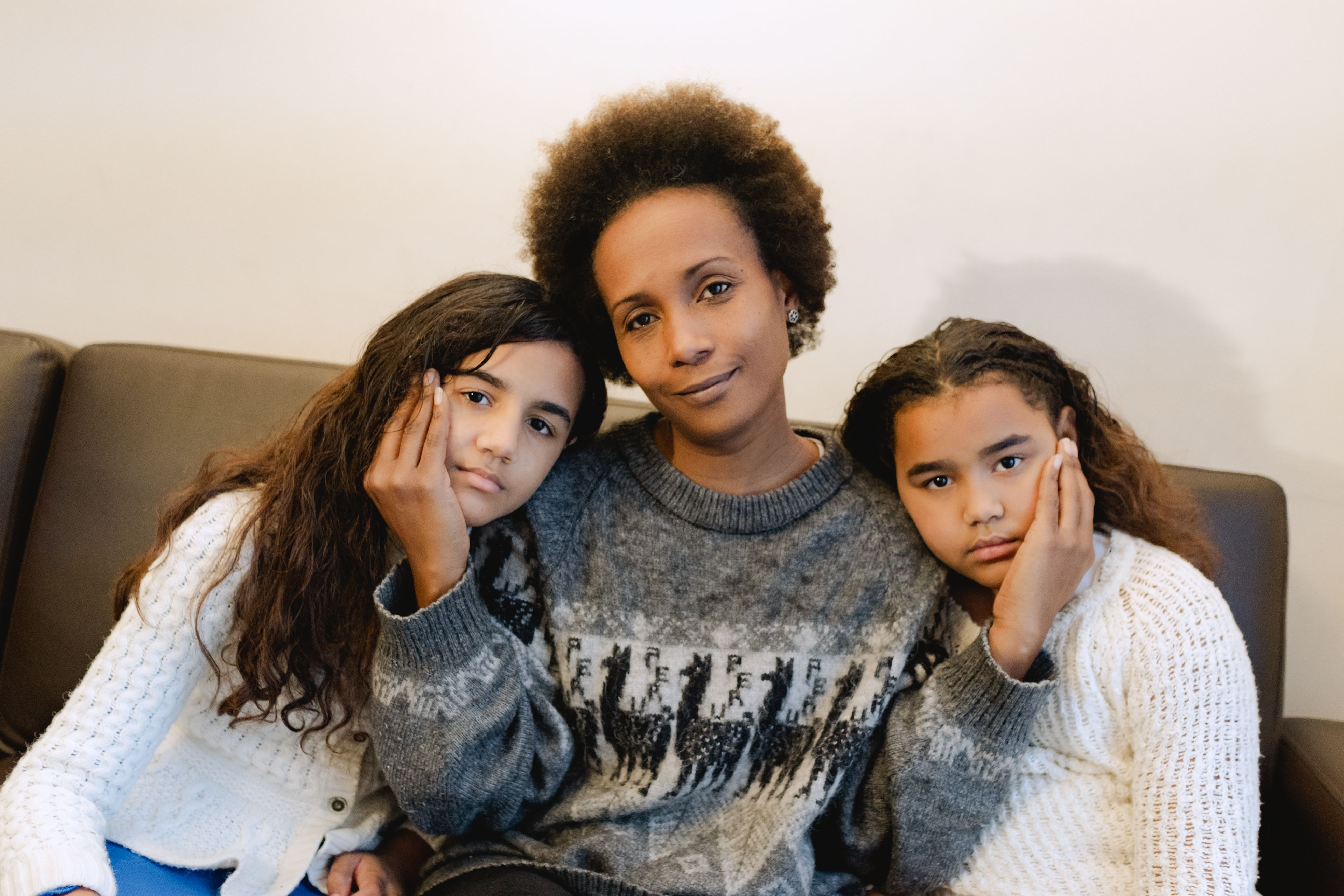 Mother and daughters share a tender moment indoors, highlighting familial bonds.