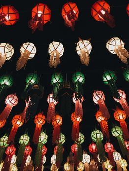 Vibrant traditional lanterns in red, green, and white illuminate the night sky during a festival in Thailand.