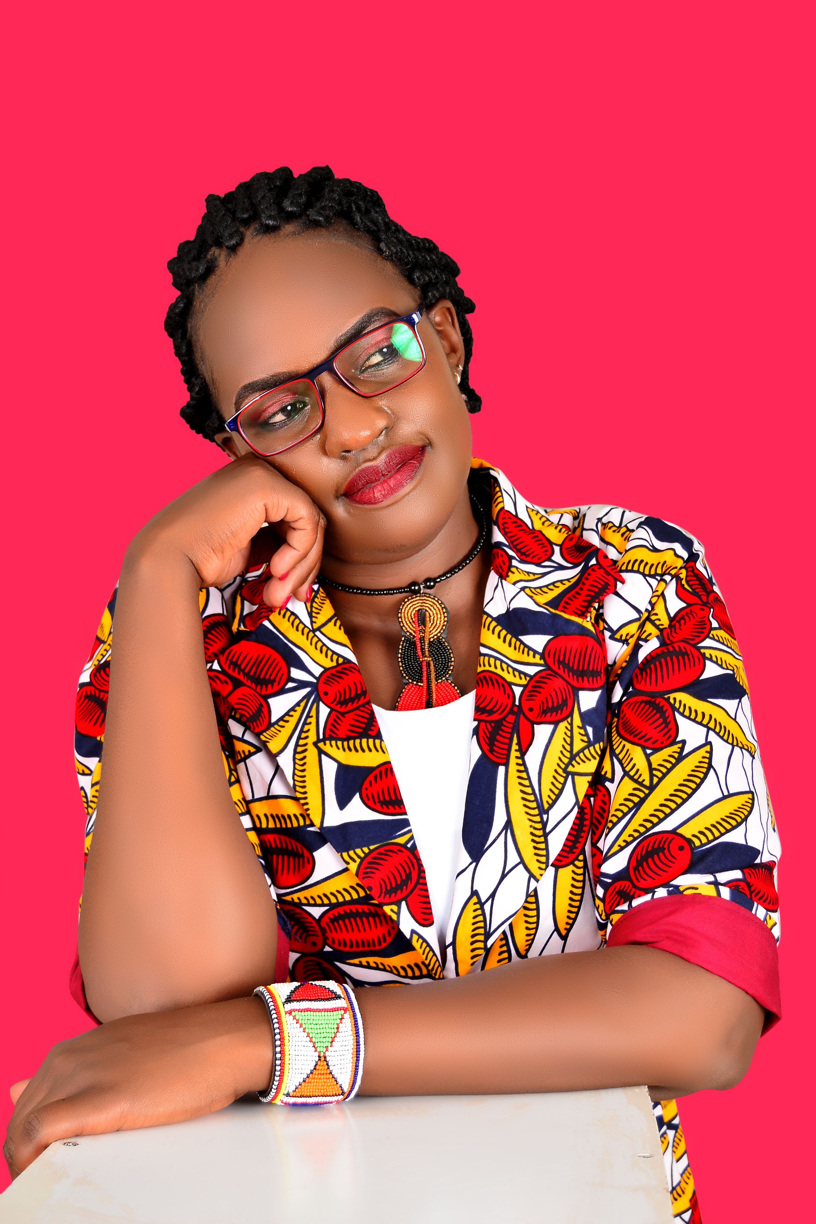 A fashionable woman poses indoors with a vibrant red background, wearing a stylish African print outfit.