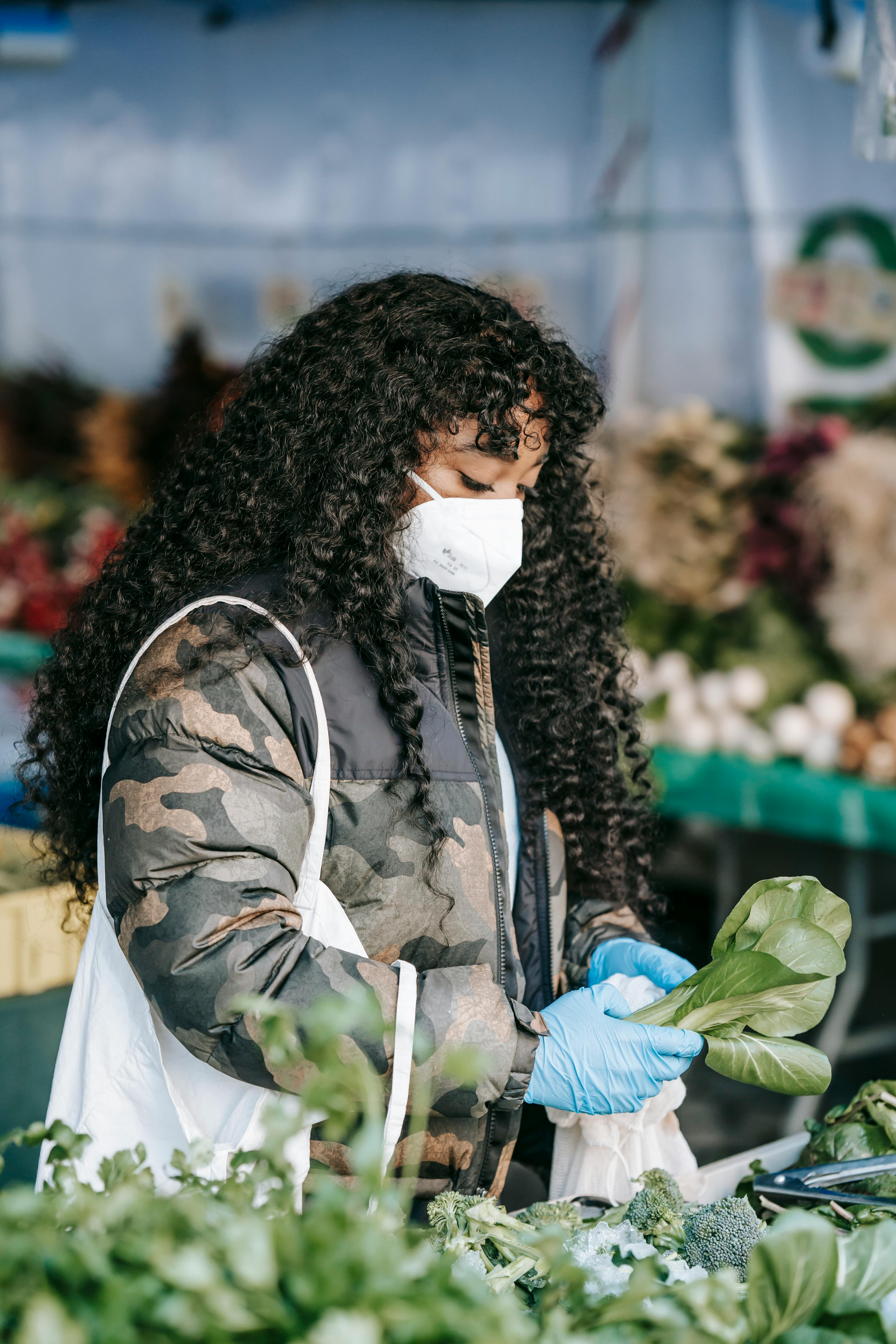 woman in protective mask buying spinach in market