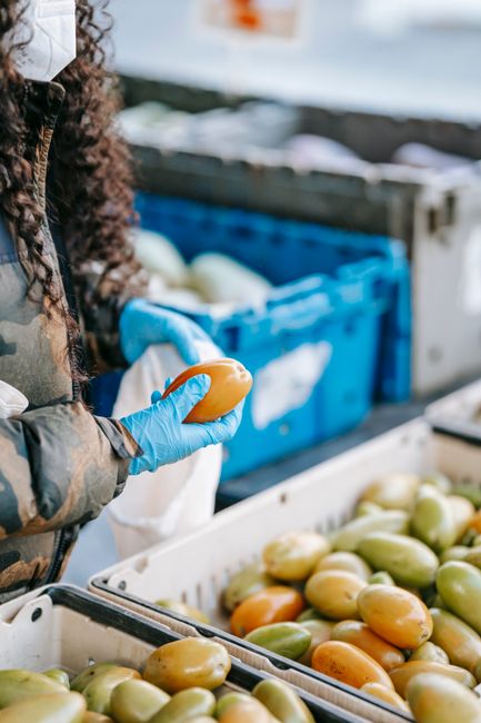 Photo by Uriel Mont Crop anonymous female buyer picking green tomatoes while shopping in grocery store in gloves and protective mask