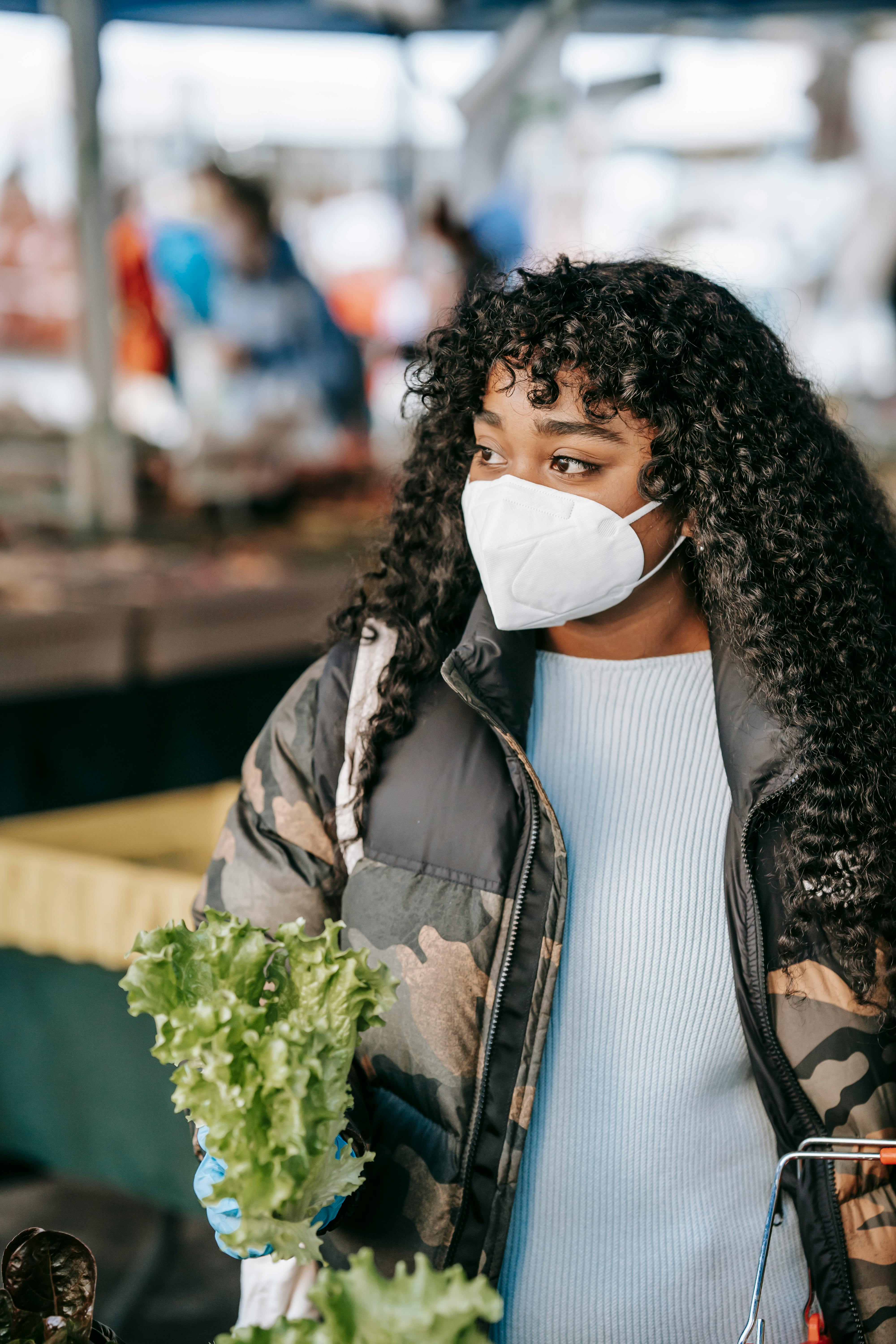 young black woman in mask buying lettuce in market