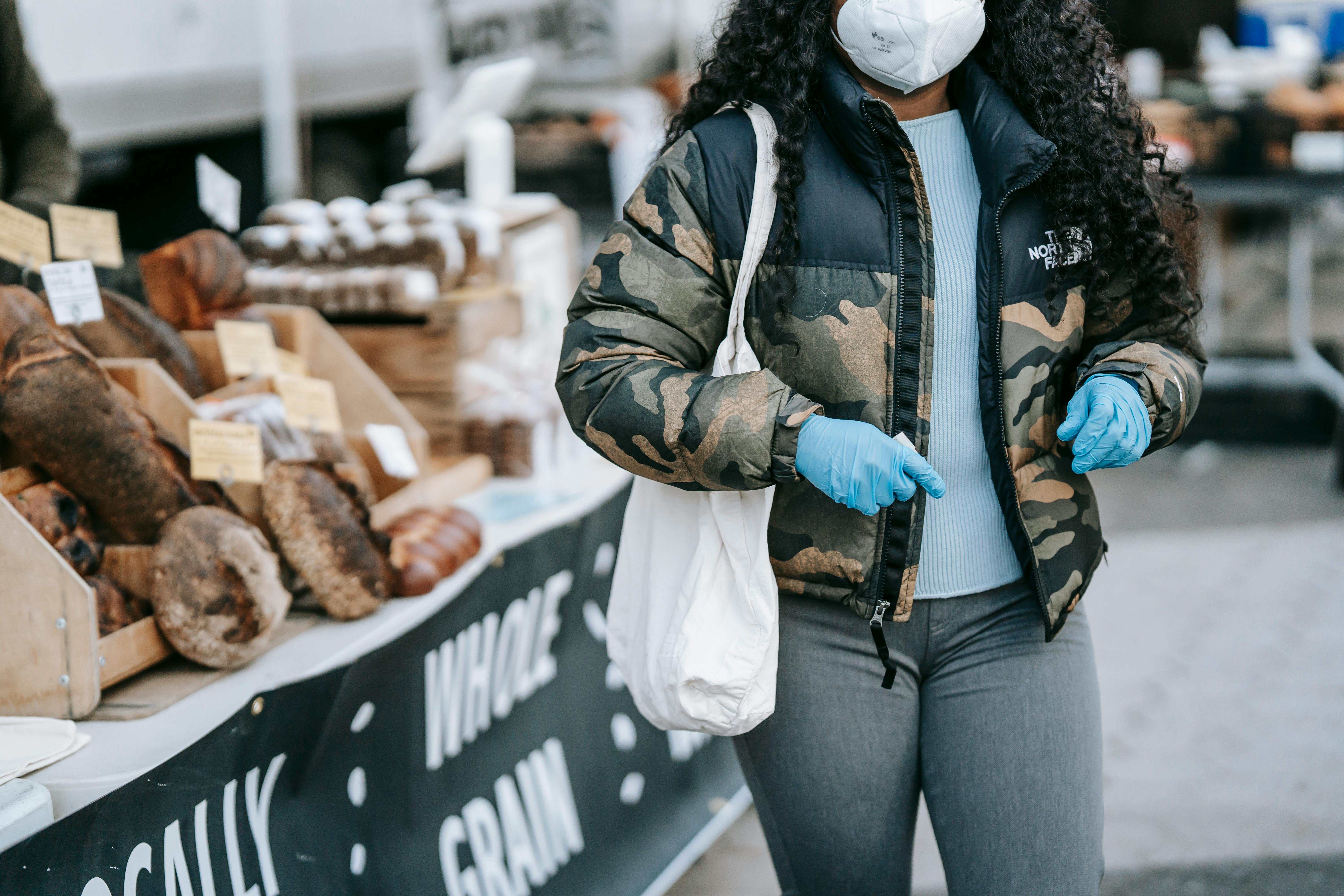 black woman in mask walking by street bakery