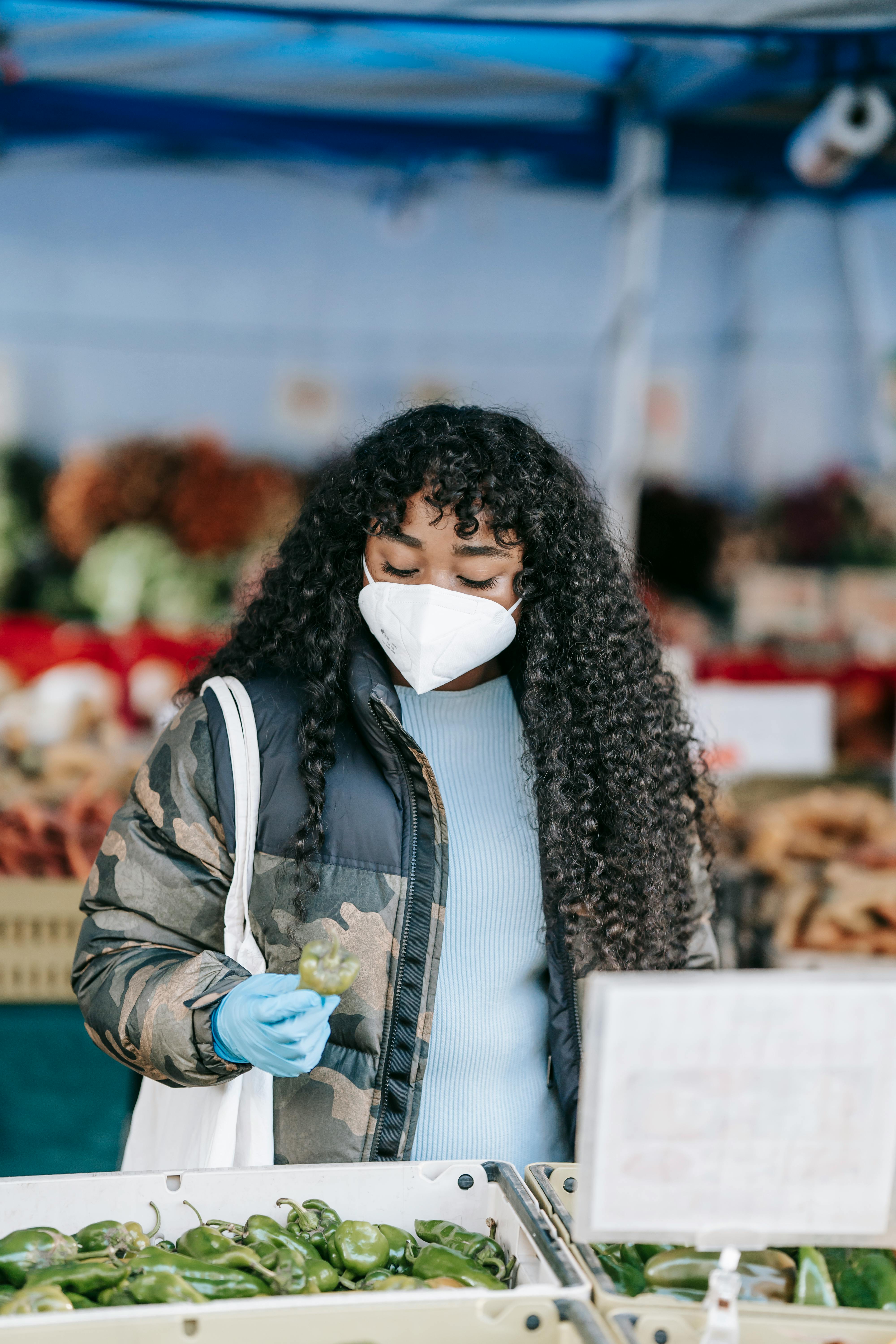 black woman in medical mask choosing anaheim pepper