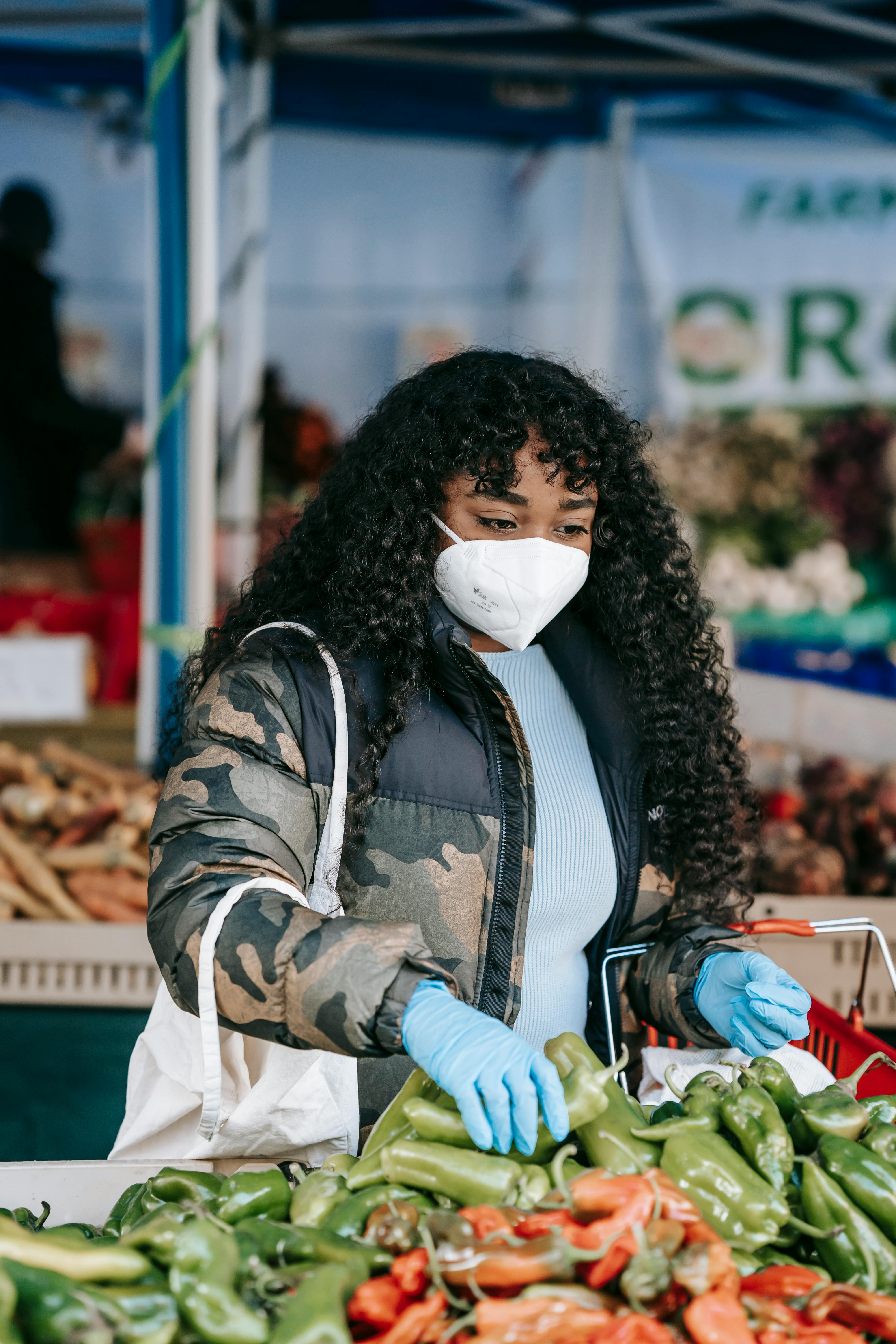 black woman in protective mask picking anaheim pepper