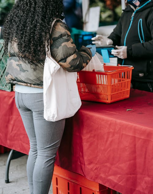 Frau In Weißer Jacke Und Blauer Jeans, Die Neben Rotem Plastikkorb Stehen