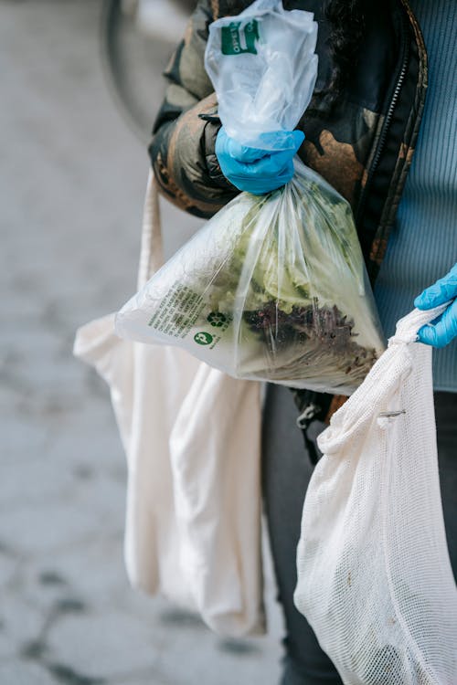 Crop unrecognizable person in gloves putting vegetables in shopping bag
