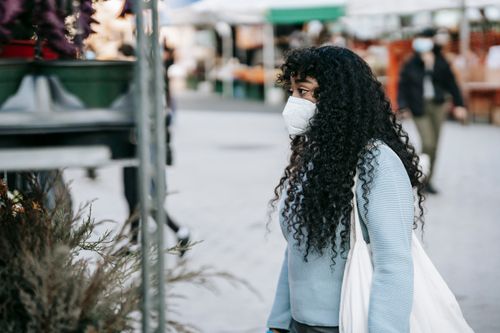 Free Side view focused African American female in casual clothes and mask choosing potted flowers represented on shelves in local street market Stock Photo