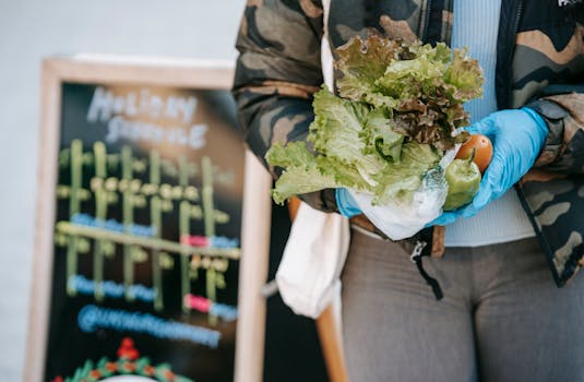 A close-up of a woman with gloves holding fresh vegetables at an outdoor market.