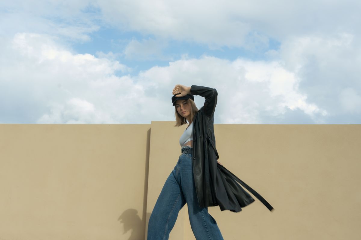 A woman in a leather trench coat near a yellow wall — denim styled with outerwear