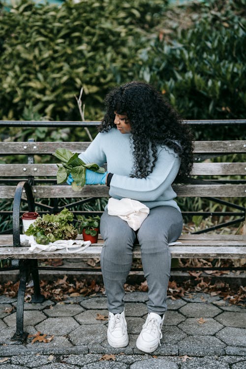 Black female sitting on bench and taking cafe of plants in garden