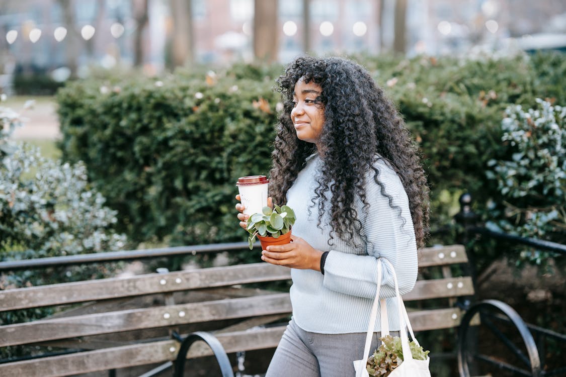 Free Black woman in park with takeaway drink and potted plant Stock Photo