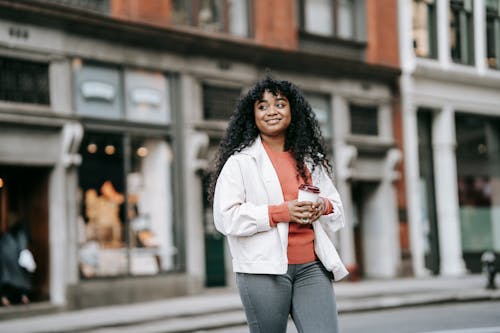 Cheerful black woman with takeaway coffee walking on street