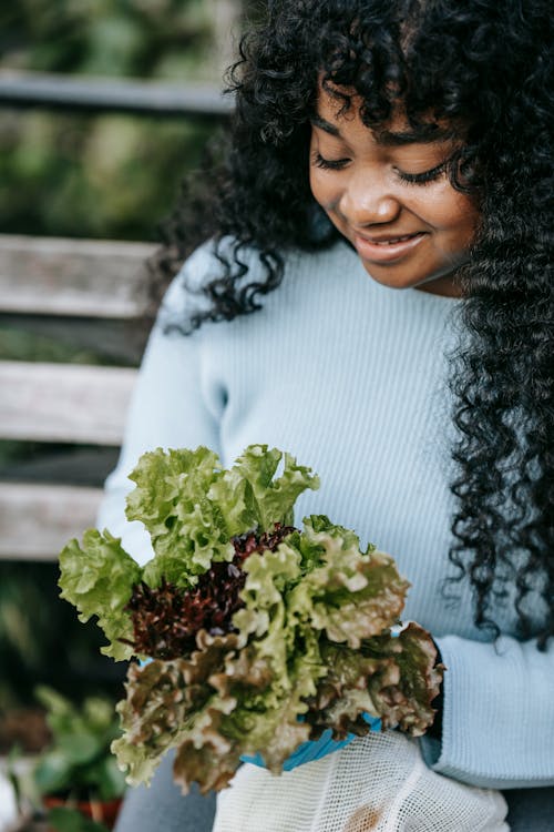 Crop black woman holding lettuce salad in park