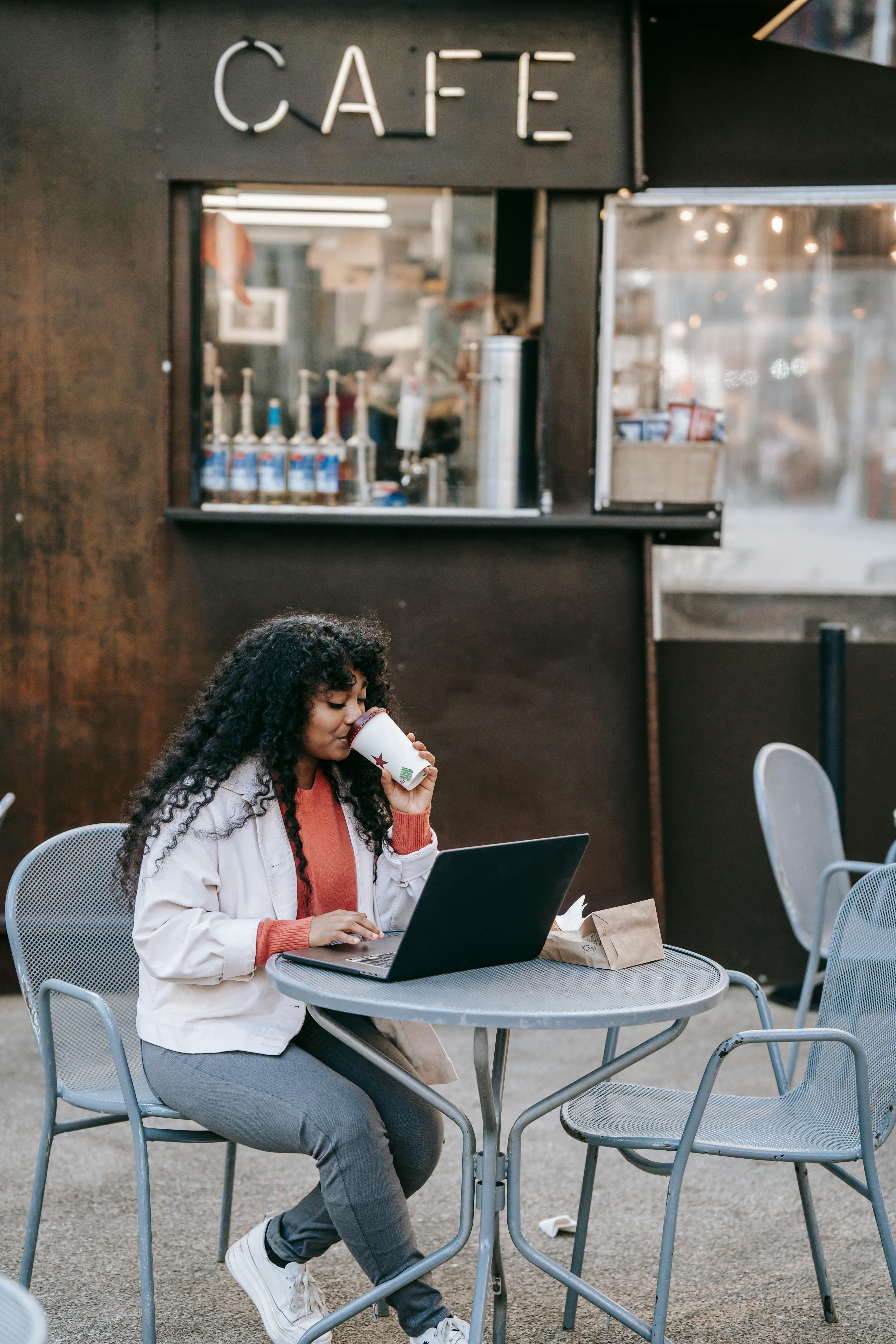 black woman drinking coffee and using laptop in street cafe