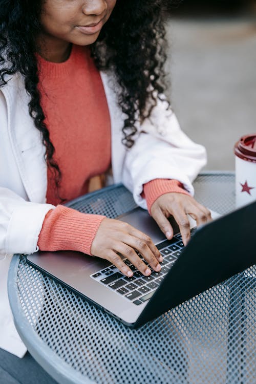 Free Crop calm African American female wearing casual outfit browsing modern netbook while having coffee break in outdoor cafeteria Stock Photo