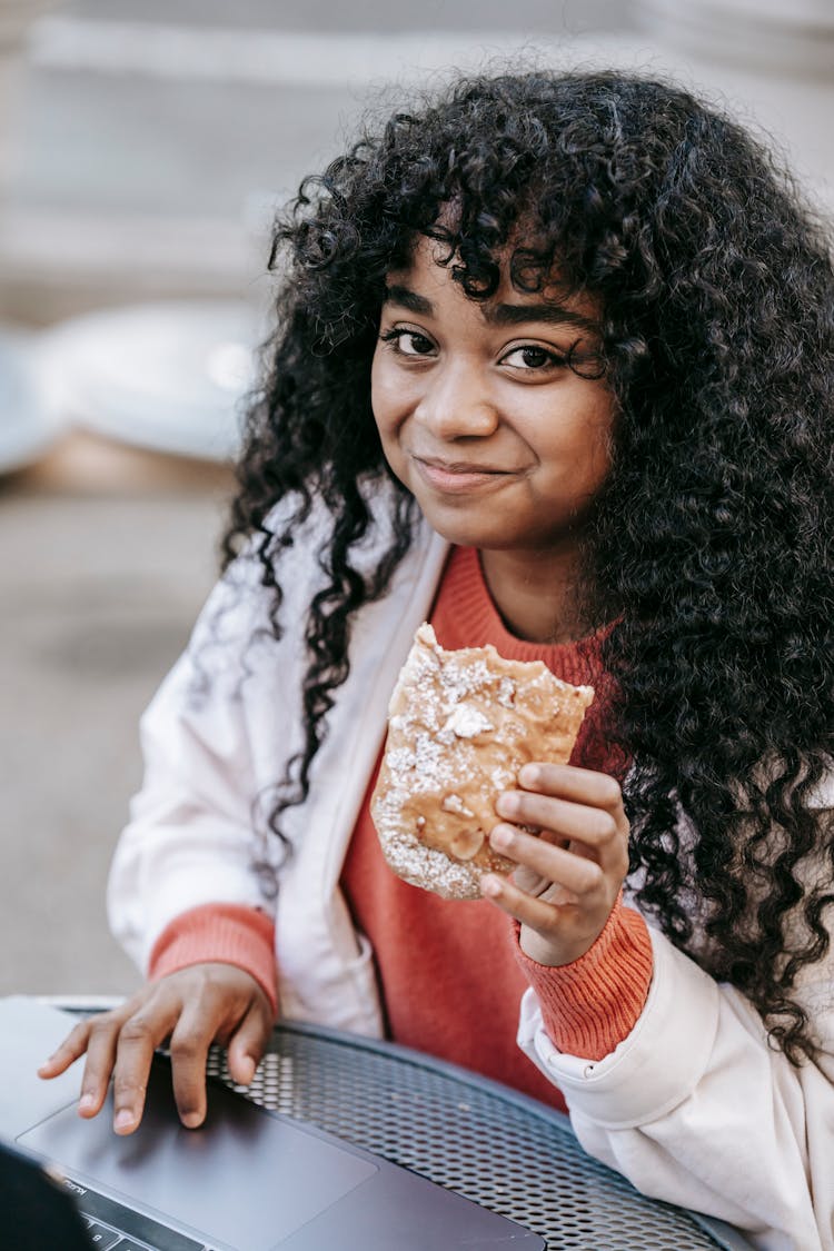 Black Woman Using Laptop And Eating Sandwich In Street Cafe