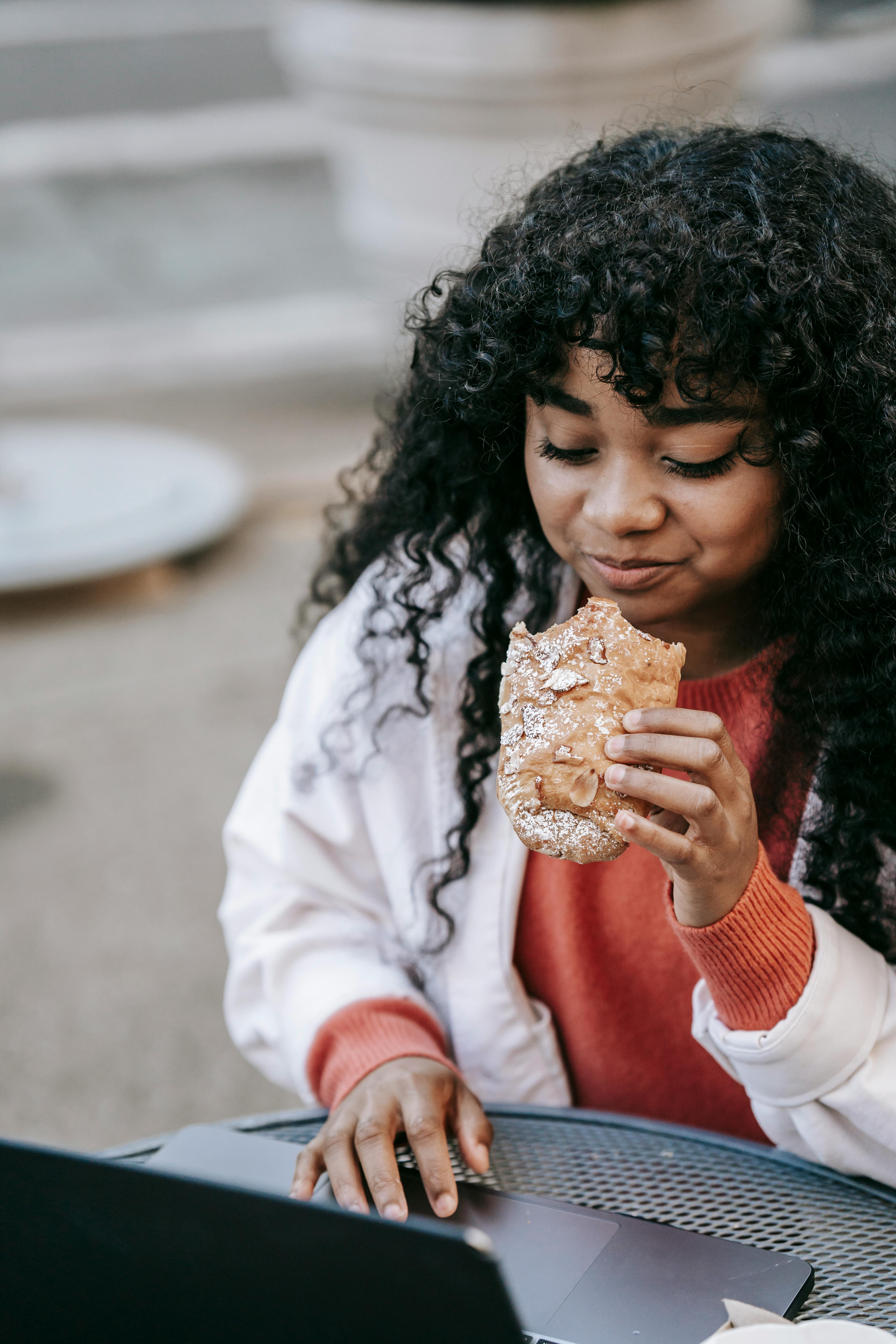 black woman eating sandwich and browsing laptop in street cafeteria