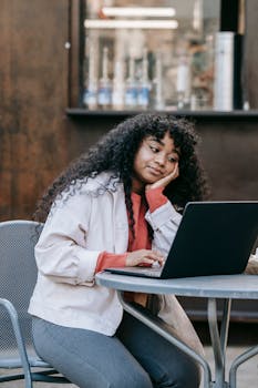 Thoughtful woman with curly hair concentrating on her laptop in a casual café setting.