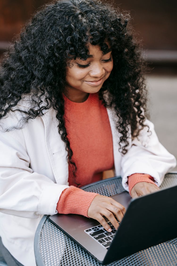 Smiling Black Woman Browsing Laptop In Street Cafe