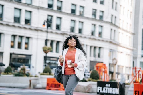 Happy black woman with takeaway coffee and sandwich on street