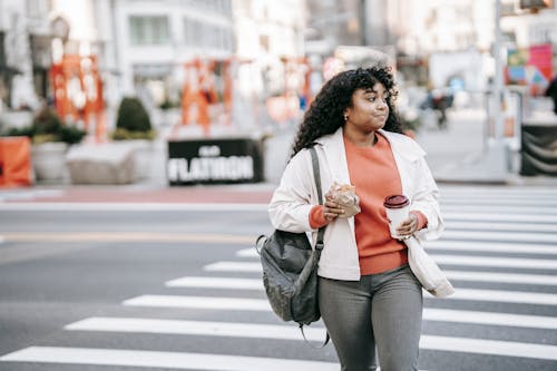 Friendly black woman with takeaway coffee crossing road in city