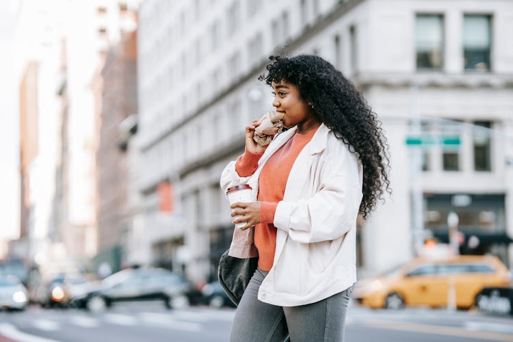 Black Woman Biting Sandwich And Crossing Road