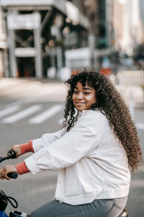 Free Side view cheerful African American female with curly hair riding bicycle on city street and looking away happily Stock Photo