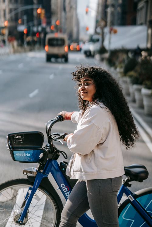 Free Side view glad African American female in casual outfit with bicycle crossing road in modern city Stock Photo