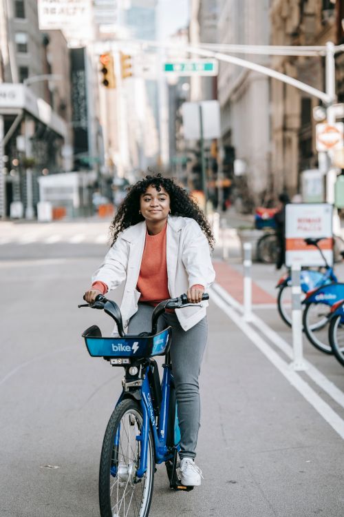 Free Full length of young black lady in casual outfit riding bicycle on asphalt road on street in town near buildings in sunny day Stock Photo