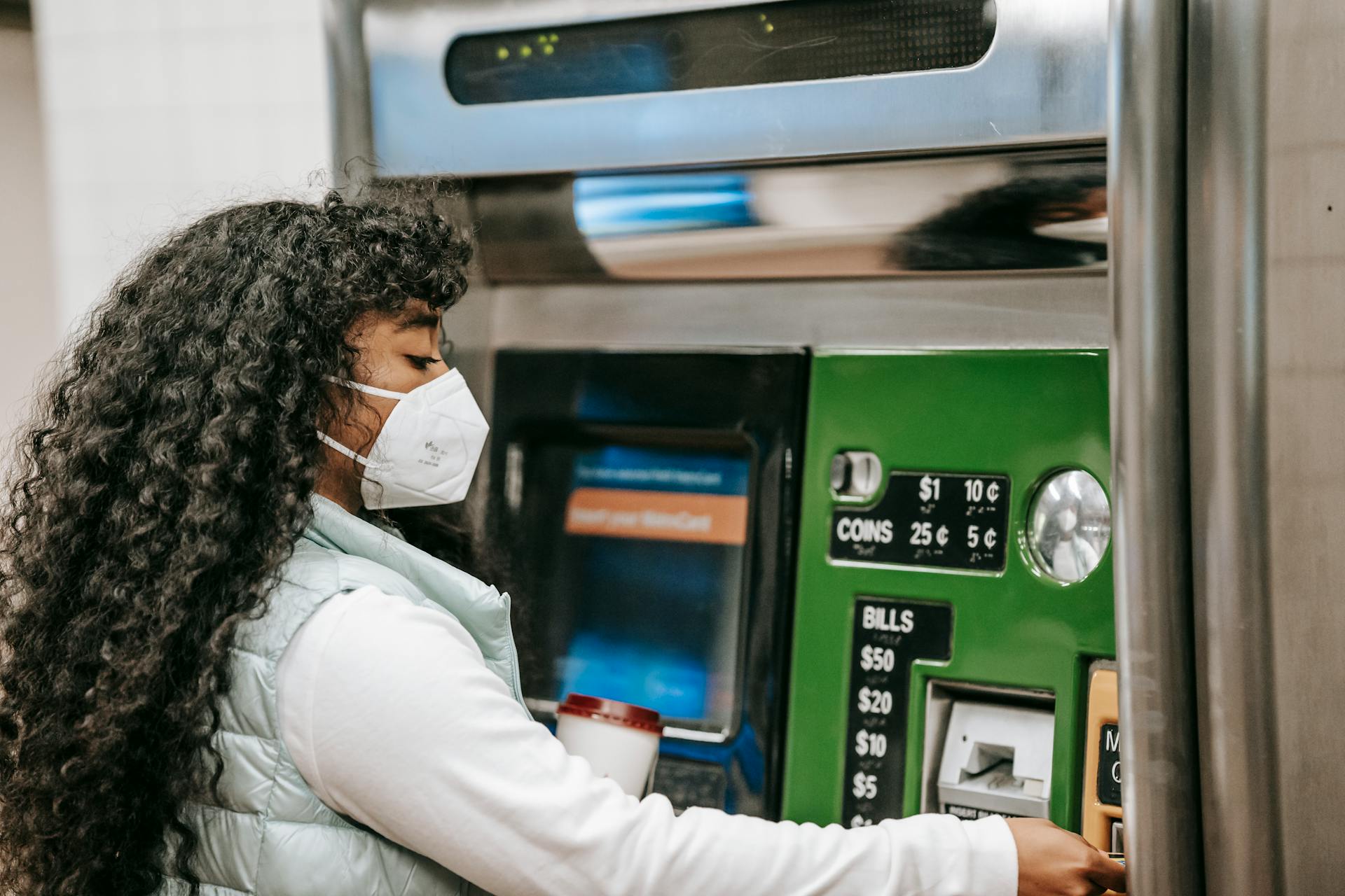 A woman wearing a face mask uses a ticket machine for purchasing fare in a public setting, reflecting safety during pandemic times.